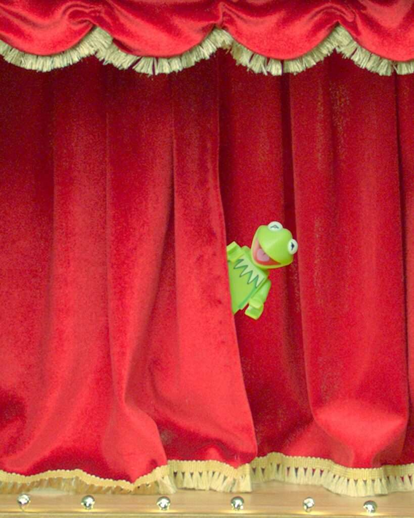 Lego Kermit minifig peeking out from behind a red curtain